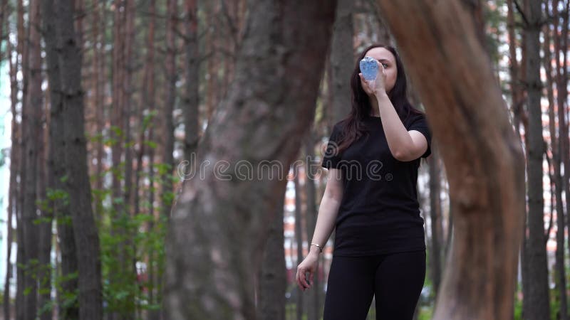 Γυναίκα στη μαύρη αθλητική ενδυμασία στα ξύλα ή πάρκο, πόσιμο νερό από ένα μπουκάλι μετά από ένα τρέξιμο