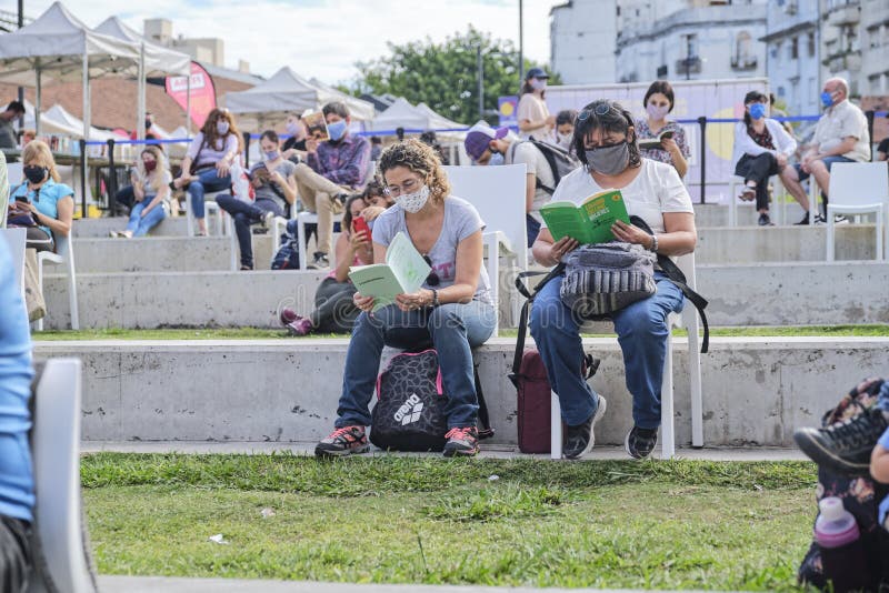 Buenos Aires, Argentina; April 2, 2021: women sitting outdoors at a reading activity, using masks and keeping distance for the prevention of covid, during the Felba, Publishers and Bookstores Fair. Buenos Aires, Argentina; April 2, 2021: women sitting outdoors at a reading activity, using masks and keeping distance for the prevention of covid, during the Felba, Publishers and Bookstores Fair