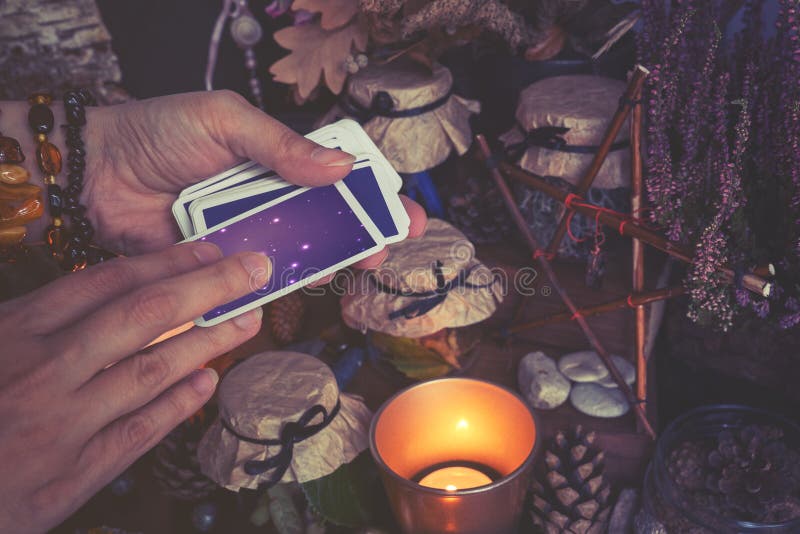 Woman hand is holding deck of tarot or oracle cards performing fortunetelling. Toned to cold colors in shadows. Woman hand is holding deck of tarot or oracle cards performing fortunetelling. Toned to cold colors in shadows