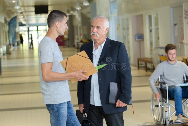 Δάσκαλος γυμνασίου που μιλά στον άνδρα σπουδαστή έξω από την τάξη στοκ φωτογραφία με δικαίωμα ελεύθερης χρήσης Δάσκαλος γυμνασίου που μιλά στον άνδρα σπουδαστή έξω από την τάξη στοκ φωτογραφία με δικαίωμα ελεύθερης χρήσης
