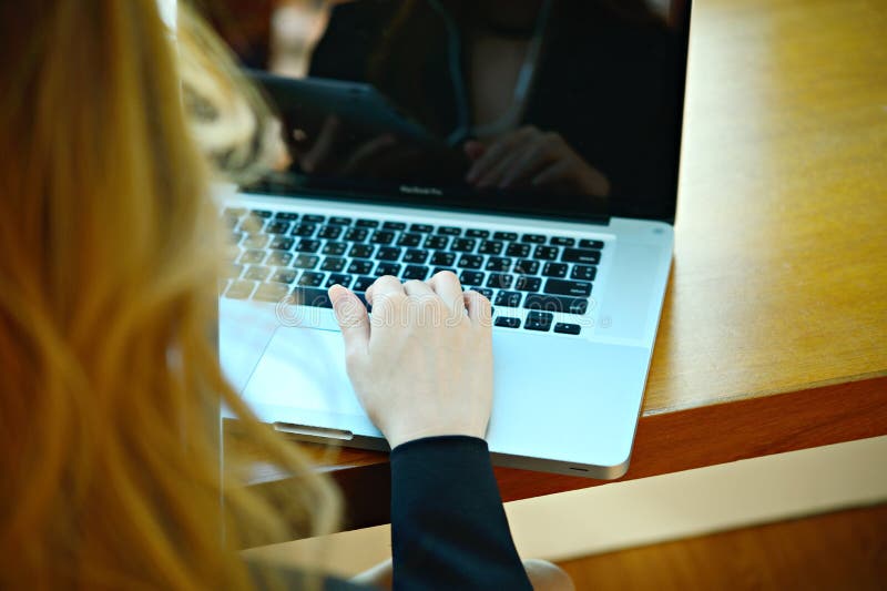 Δίνει μια γυναίκα στο lap-top πληκτρολογίων ή netbook τη συνεδρίαση στα des της στοκ εικόνα