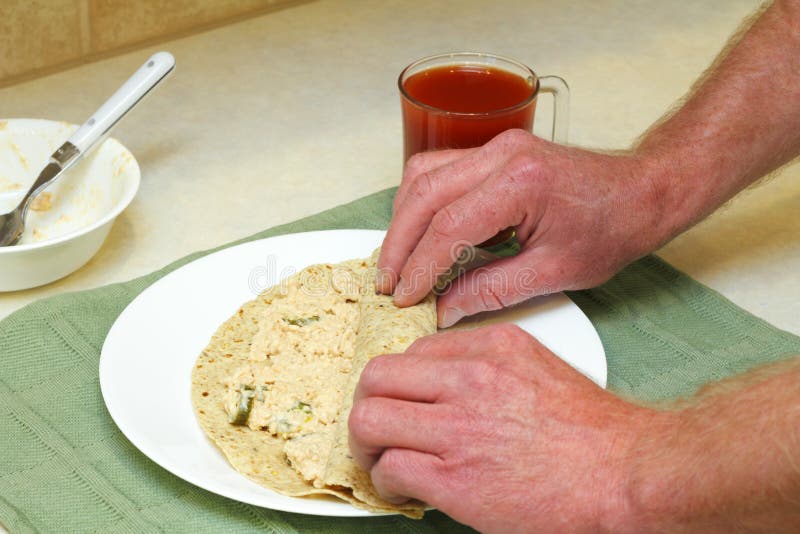 Male hands rolling up salmon salad with jalapenos in a multi-grain soft tortilla for lunch. Male hands rolling up salmon salad with jalapenos in a multi-grain soft tortilla for lunch.