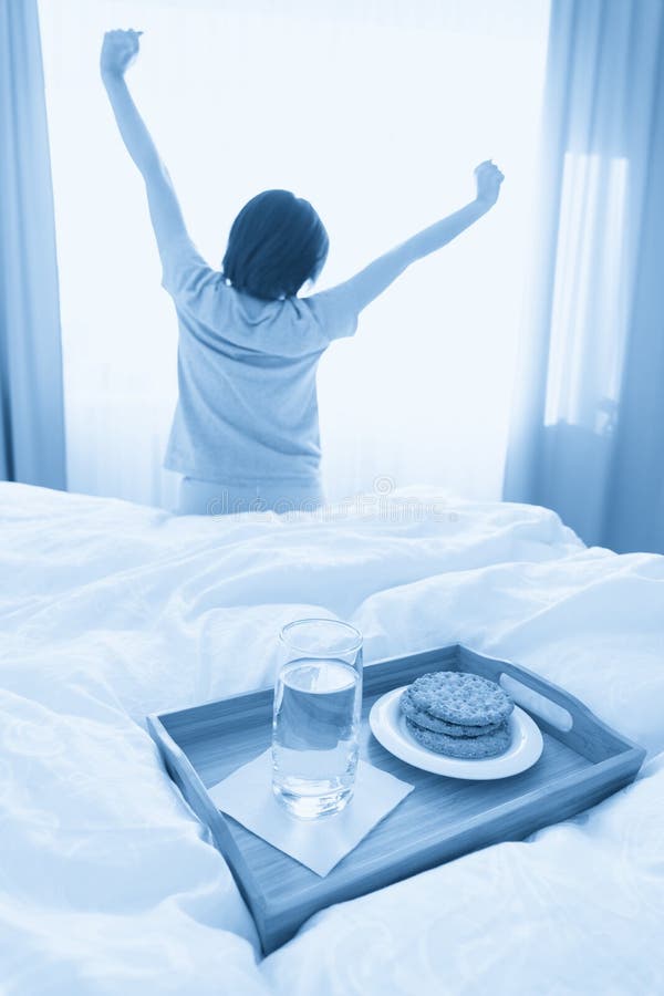 δίσκος με νερό και κρακεράκια πρωινό σε ένα κρεβάτι με γυναίκα που εκτείνεται στο φόντο