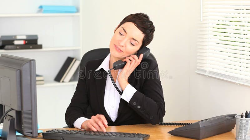 Δακτυλογράφηση γυναικών Brunette σε ένα lap-top και απάντηση του τηλεφώνου απόθεμα βίντεο