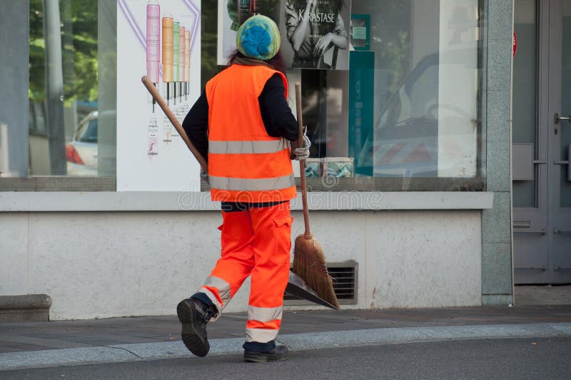 Δημοτικός υπάλληλος γυναικών που περπατά με το φτυάρι και τη σκούπα υπό εξέταση στοκ φωτογραφία με δικαίωμα ελεύθερης χρήσης Δημοτικός υπάλληλος γυναικών που περπατά με το φτυάρι και τη σκούπα υπό εξέταση στοκ φωτογραφία με δικαίωμα ελεύθερης χρήσης