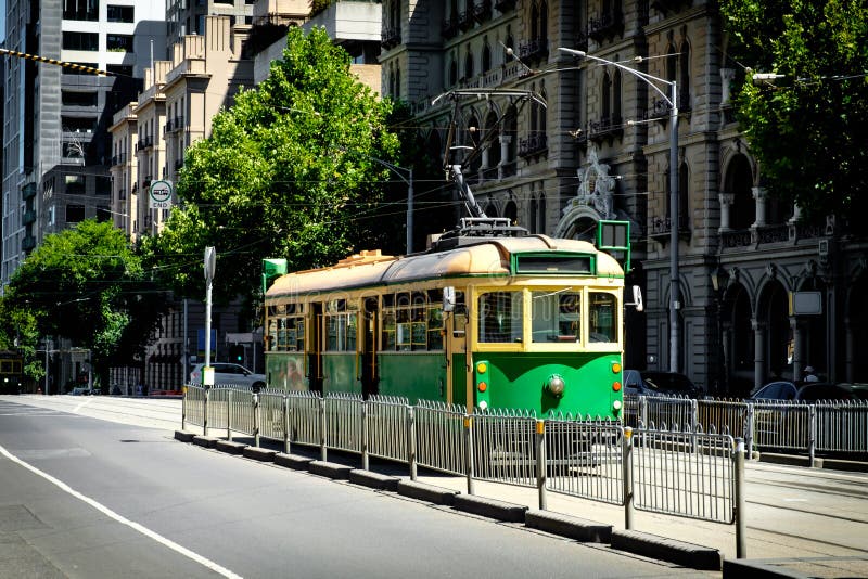 Melbourne, Australia - January 1, 2020: Popular classic yellow-green city cycle trams moving on the tramway with a group of tourists nearby. Melbourne, Australia - January 1, 2020: Popular classic yellow-green city cycle trams moving on the tramway with a group of tourists nearby
