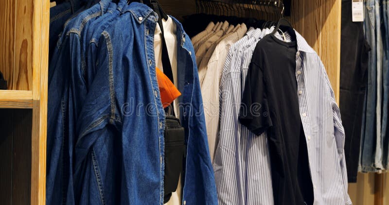 Διάφορα μπλουζάκια και μπλουζάκια για denim κρέμονται σε κρεμάστρες ρούχων σε ένα κατάστημα λιανικής που παρουσιάζουν μια σειρά στ στοκ φωτογραφίες