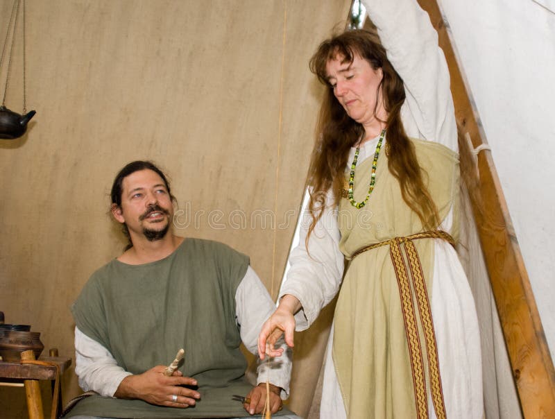 Farmer and his wife in middle ages during a camp. she is making yarn by hand. Farmer and his wife in middle ages during a camp. she is making yarn by hand