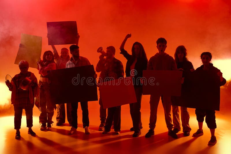 Διαδηλωτές υπό κόκκινο φως με αφίσες που κρατούν ομίχλη και φωνάζουν μαζί. Μερικοί σηκώνουν γροθιές άλλοι χτυπούν κατσαρόλες. Επίδ στοκ φωτογραφία