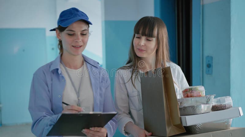 διαδικτυακή παραγγελία γυναίκα νοικοκυρά λαμβάνει ψώνια που παραδίδονται από γυναίκα ταχυδρόμο στο σπίτι της απόθεμα βίντεο