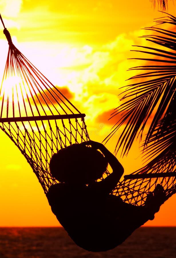 View of a woman lounging in hammock during sunset. View of a woman lounging in hammock during sunset