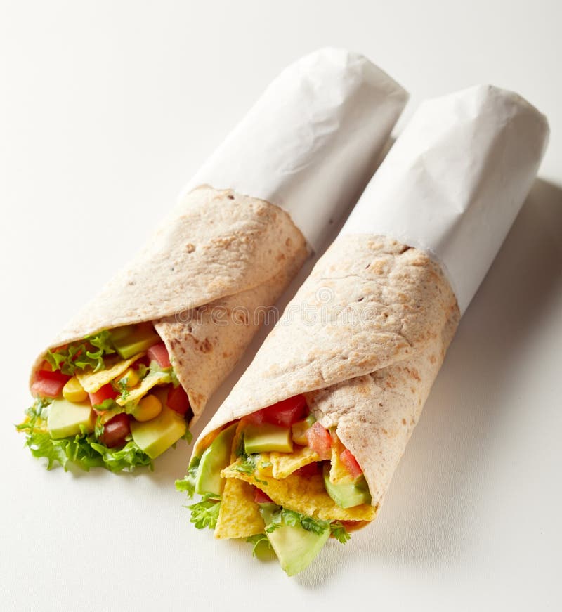 Two takeaway tortilla wraps with avocado pear, nachos, chili peppers, tomato and lettuce wrapped in paper ready to go. Two takeaway tortilla wraps with avocado pear, nachos, chili peppers, tomato and lettuce wrapped in paper ready to go