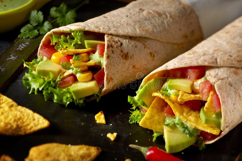 Two tortilla wraps with avocado pear, salad trimmings, chili peppers and nachos in a close up view ready to be served. Two tortilla wraps with avocado pear, salad trimmings, chili peppers and nachos in a close up view ready to be served