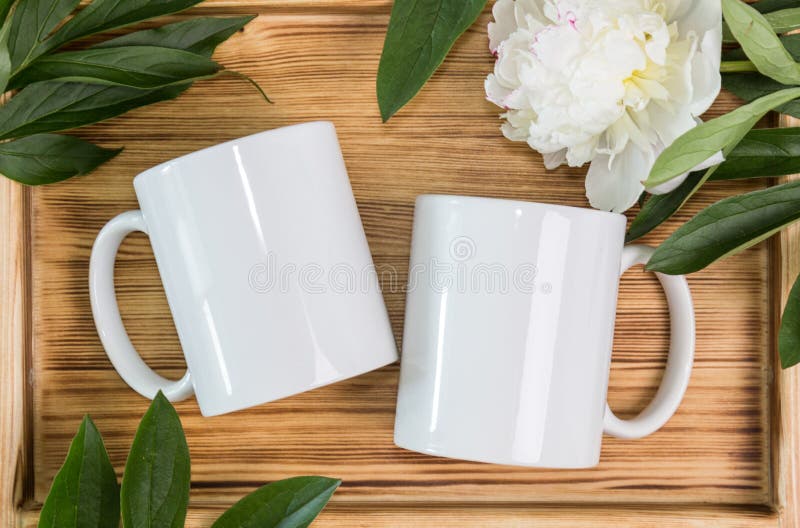 Two white mugs, cups wedding mockup. Peony, green leaves, wooden background. Summer gifts, boho style. Two white mugs, cups wedding mockup. Peony, green leaves, wooden background. Summer gifts, boho style