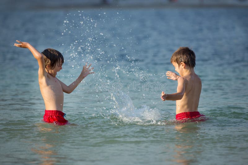 Two sweet children, boy brothers, splashing each other with water on the beach on sunset. Two sweet children, boy brothers, splashing each other with water on the beach on sunset