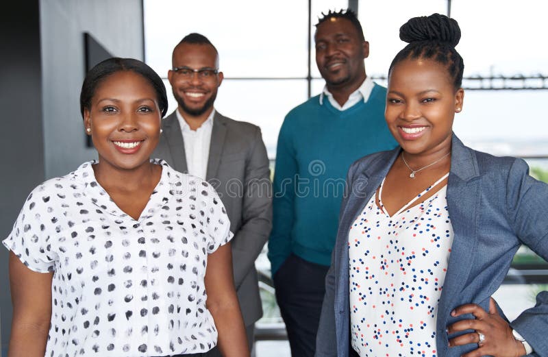 Group of four black professionals wearing fashionable corporate clothing standing confidently together in bright modern office space. Group of four black professionals wearing fashionable corporate clothing standing confidently together in bright modern office space