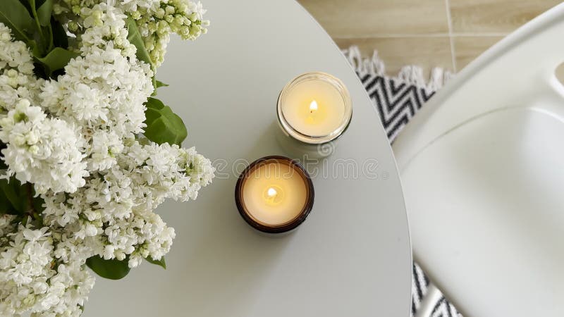 δύο κεριά που καίγονται και ένα μπουκέτο λιλά σε στρογγυλό λευκό τραπέζι σε ένα αληθινό σπιτικό μινιμαλιστικό εσωτερικό