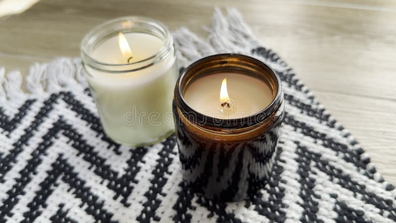 δύο κεριά που καίγονται σε γυάλινο βάζο πάνω σε μαύρο και λευκό χαλί στο δάπεδο