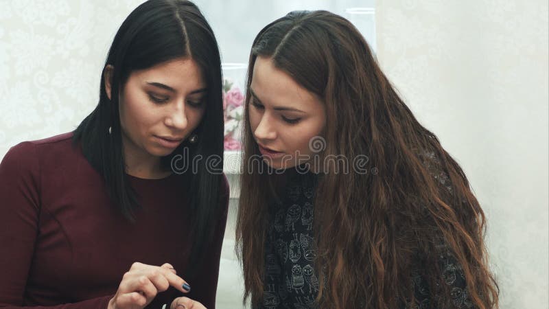 Δύο κορίτσια χρησιμοποιούν ένα smartphone, ομιλία, χαμόγελο, που κάθεται στον καναπέ φιλμ μικρού μήκους
