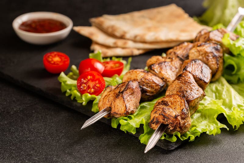 δύο μερίδες shish kebab σε ένα πέτρινο πιάτο με σαλάτα.