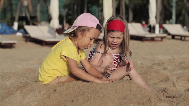 Δύο μικρά χαριτωμένα κορίτσια που παίζουν με την άμμο στην παραλία