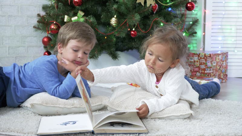 Δύο μικροί χαριτωμένοι αμφιθαλείς που διαβάζουν ένα βιβλίο στο πάτωμα κοντά στο χριστουγεννιάτικο δέντρο