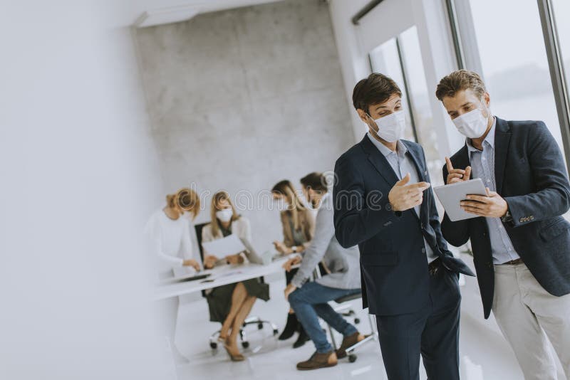 δύο νεαροί επιχειρηματίες με προστατευτικές μάσκες προσώπου και συζήτηση με σχέδιο στο γραφείο στοκ φωτογραφία