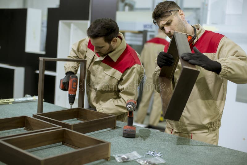 Δύο νεαροί εργάτες συναρμολογούν έπιπλα στο εργοστάσιο στοκ εικόνες