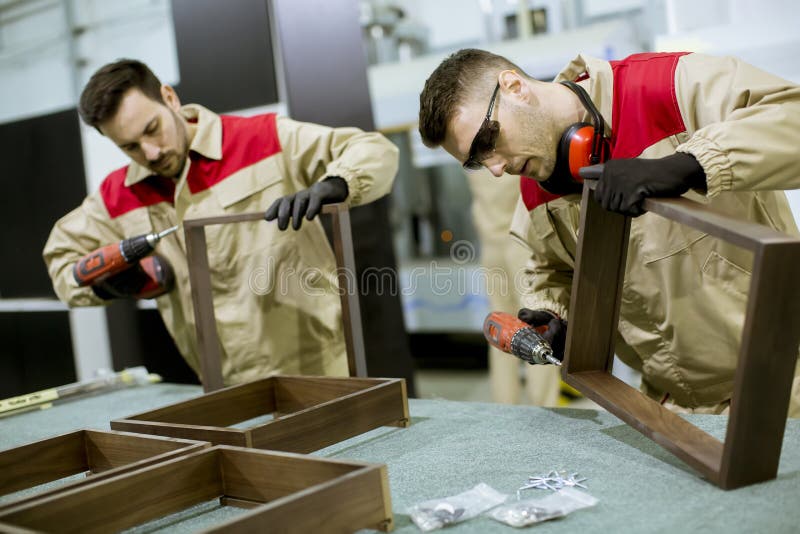 Δύο νεαροί εργάτες συναρμολογούν έπιπλα στο εργοστάσιο στοκ εικόνα με δικαίωμα ελεύθερης χρήσης