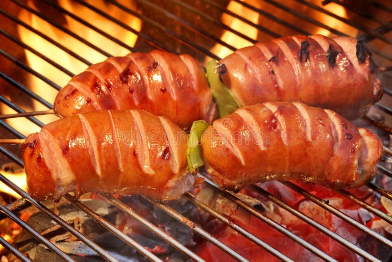 Close-up Of Two Skewers With Sausage On The Hot BBQ Charcoal Grill And Flames In The Background. Close-up Of Two Skewers With Sausage On The Hot BBQ Charcoal Grill And Flames In The Background