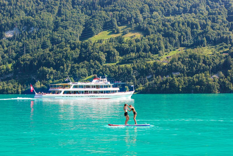 Δύο φίλοι νέων κοριτσιών που στέκονται στο paddleboard στην τυρκουάζ λίμνη Brienz στην Ελβετία Βάρκα τουριστών στο υπόβαθρο r στοκ φωτογραφίες Δύο φίλοι νέων κοριτσιών που στέκονται στο paddleboard στην τυρκουάζ λίμνη Brienz στην Ελβετία Βάρκα τουριστών στο υπόβαθρο r στοκ φωτογραφίες