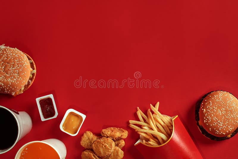 Δύο χάμπουργκερ και τηγανιτές πατάτες, σάλτσες και ποτά στο κόκκινο υπόβαθρο Γρήγορο φαγητό Η τοπ άποψη, επίπεδη βάζει με το copy