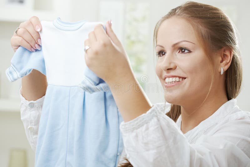 Portrait of a happy young pregnant woman holding a blue baby dress for her unborn child. Portrait of a happy young pregnant woman holding a blue baby dress for her unborn child.