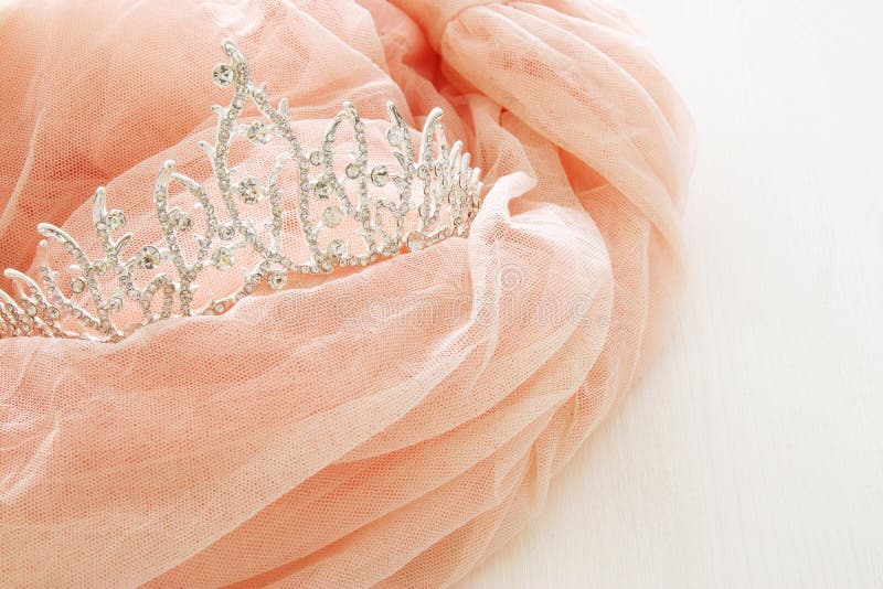 Vintage tulle pink chiffon dress and diamond tiara on wooden white table. Wedding and girl& x27;s party concept. Vintage tulle pink chiffon dress and diamond tiara on wooden white table. Wedding and girl& x27;s party concept