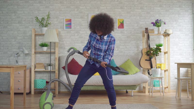 Εκφραστική θετική νοικοκυρά γυναικών αφροαμερικάνων νέα που σκουπίζει και που παίζει τη φανταστική κιθάρα με ηλεκτρική σκούπα