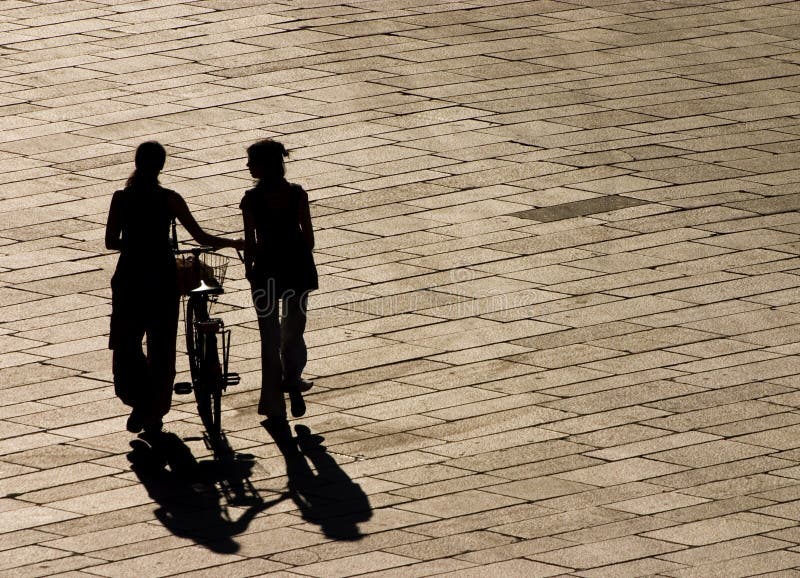 Two girls walking in a square in front of the sun light. Two girls walking in a square in front of the sun light