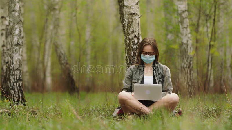 ελεύθερος επαγγελματίας κατά τη διάρκεια της καραντίνας. γυναίκα με μάσκα εργάζεται σε φορητό υπολογιστή στο δάσος