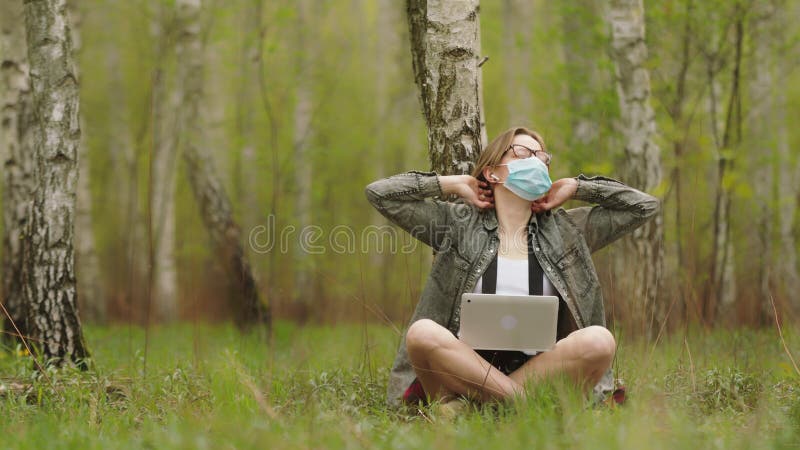 ελεύθερος επαγγελματίας κατά τη διάρκεια της καραντίνας. γυναίκα με μάσκα εργάζεται σε φορητό υπολογιστή στο δάσος
