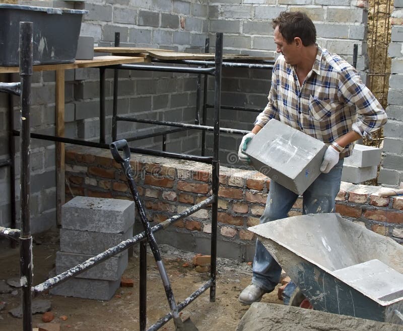A house builder lifting a heavy grey block or blocks from a wheelbarrow. A house builder lifting a heavy grey block or blocks from a wheelbarrow.