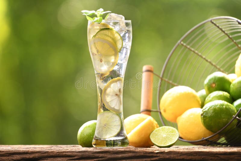 Infused water with lime and lemon in tall glass on wood and nature background. Infused water with lime and lemon in tall glass on wood and nature background