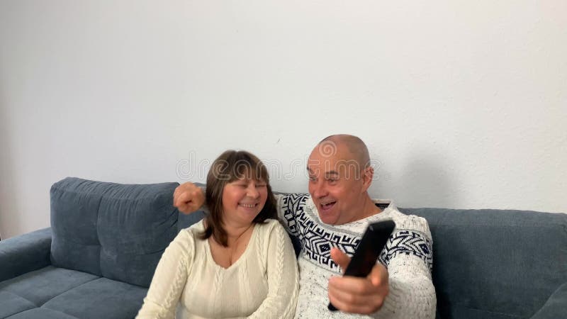 ενήλικας με σκανδιναβικό λευκό πουλόβερ και γυναίκα που κάθεται στον καναπέ και παρακολουθεί τηλεοπτική εκπομπή