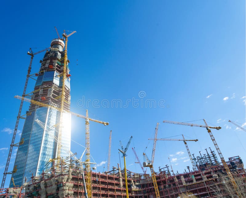 Ενεργό κτήριο ουρανοξυστών κλίμακας, έντονο φως από τον ήλιο στα παράθυρα, γερανοί ενάντια στο μπλε ουρανό στοκ φωτογραφία με δικαίωμα ελεύθερης χρήσης Ενεργό κτήριο ουρανοξυστών κλίμακας, έντονο φως από τον ήλιο στα παράθυρα, γερανοί ενάντια στο μπλε ουρανό στοκ φωτογραφία με δικαίωμα ελεύθερης χρήσης