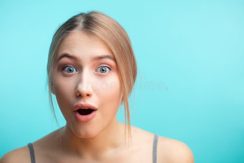 Macro shot of surprised caucasian woman over blue background looking at camera with astonishment as if she knew a terrifying news. Macro shot of surprised caucasian woman over blue background looking at camera with astonishment as if she knew a terrifying news