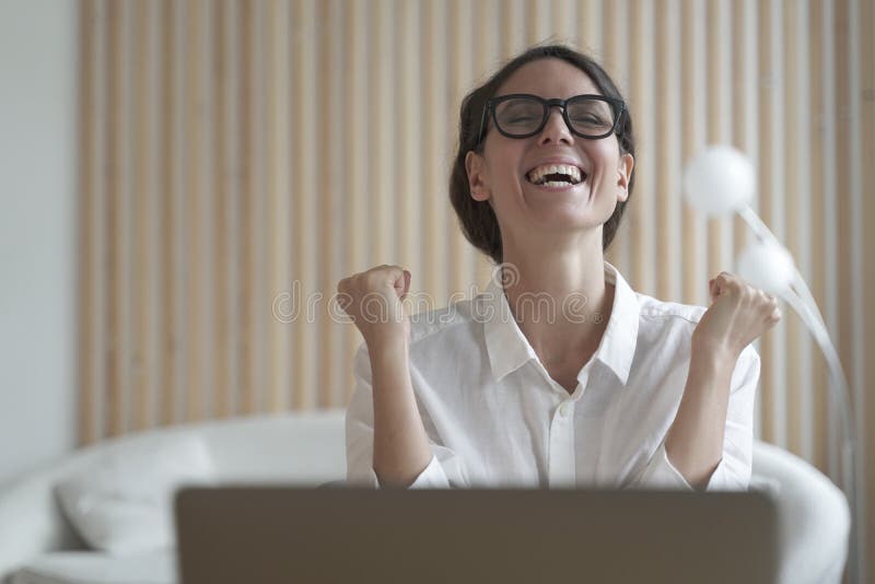 Excited latina woman freelancer clenched her fists with joy and delight with head raised up as if shouting hurray, celebrates joy of finished difficult business project. Remote work concept. Excited latina woman freelancer clenched her fists with joy and delight with head raised up as if shouting hurray, celebrates joy of finished difficult business project. Remote work concept