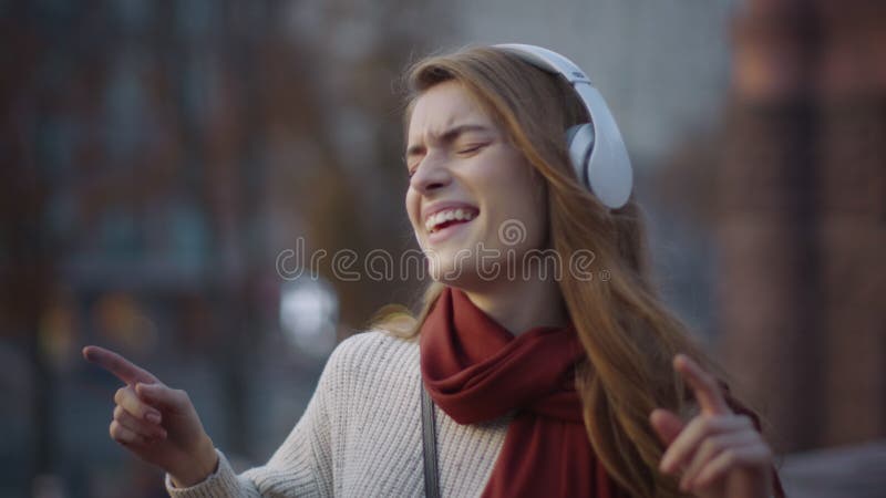 ενθουσιασμένη κοπέλα που χορεύει ακουστικά έξω. γλυκιά γυναίκα που τραγουδάει στο δρόμο της πόλης.