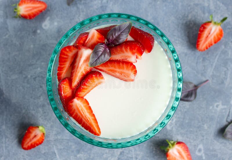 επάνω όψη της panna cotta σε γυάλα με τυρκουάζ με φέτες φρέσκων φύλλων φράουλας βασιλικού σε συγκεκριμένη επιφάνεια στοκ εικόνα