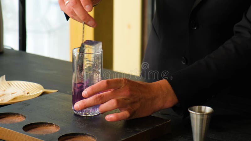 επαγγελματίας μπάρμαν ανακαλεί ένα κοκτέιλ με πάγο σε ένα διαφανές ποτήρι με ένα κουτάλι σε ένα υπαίθριο πάρτι