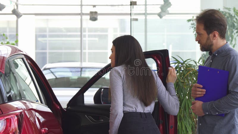 Επαγγελματική αυτοκινήτων πόρτα αυτοκινήτων εμπόρων ανοίγοντας για το θηλυκό πελάτη του στοκ εικόνα Επαγγελματική αυτοκινήτων πόρτα αυτοκινήτων εμπόρων ανοίγοντας για το θηλυκό πελάτη του στοκ εικόνα