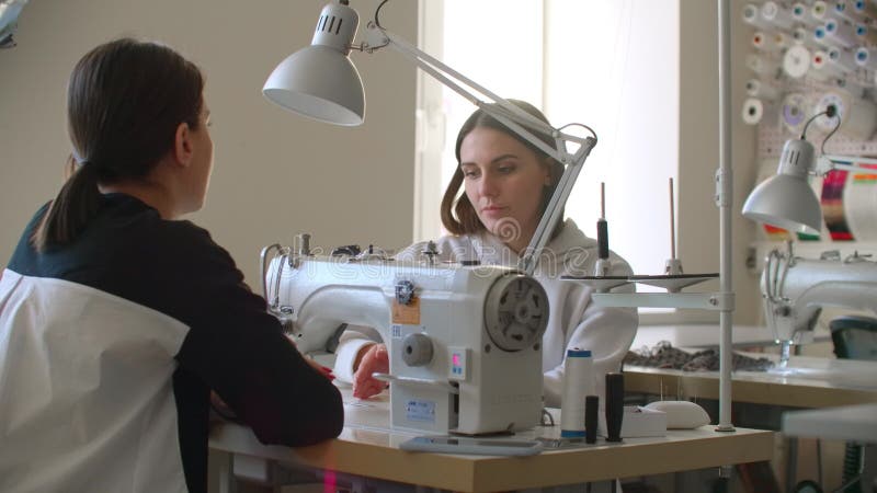 Επαγγελματική Καυκάσια μοδίστρα και νέα μοδίστρα επιλέγουν ύφασμα και μιλάνε ενώ συνεργάζονται με ραπτομηχανή απόθεμα βίντεο