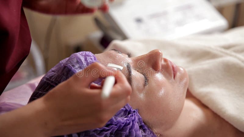 Επεξεργασία προσώπου αντι-γήρανσης με τη μάσκα προσώπου μιας γυναίκας Το cosmetologist βάζει ένα ενυδατικό πήκτωμα στο πρόσωπο με
